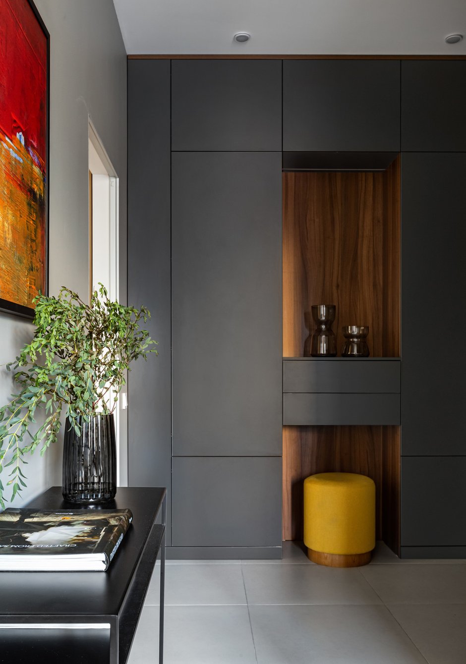 В прихожей висит яркая алая картина неизвестного автора, она тоже является важным объединяющим звеном. Если ее убрать, многое распадется и станет нелогичным. Пуф в прихожей также замыкает весь цветовой круг, который образовался в этих помещениях.