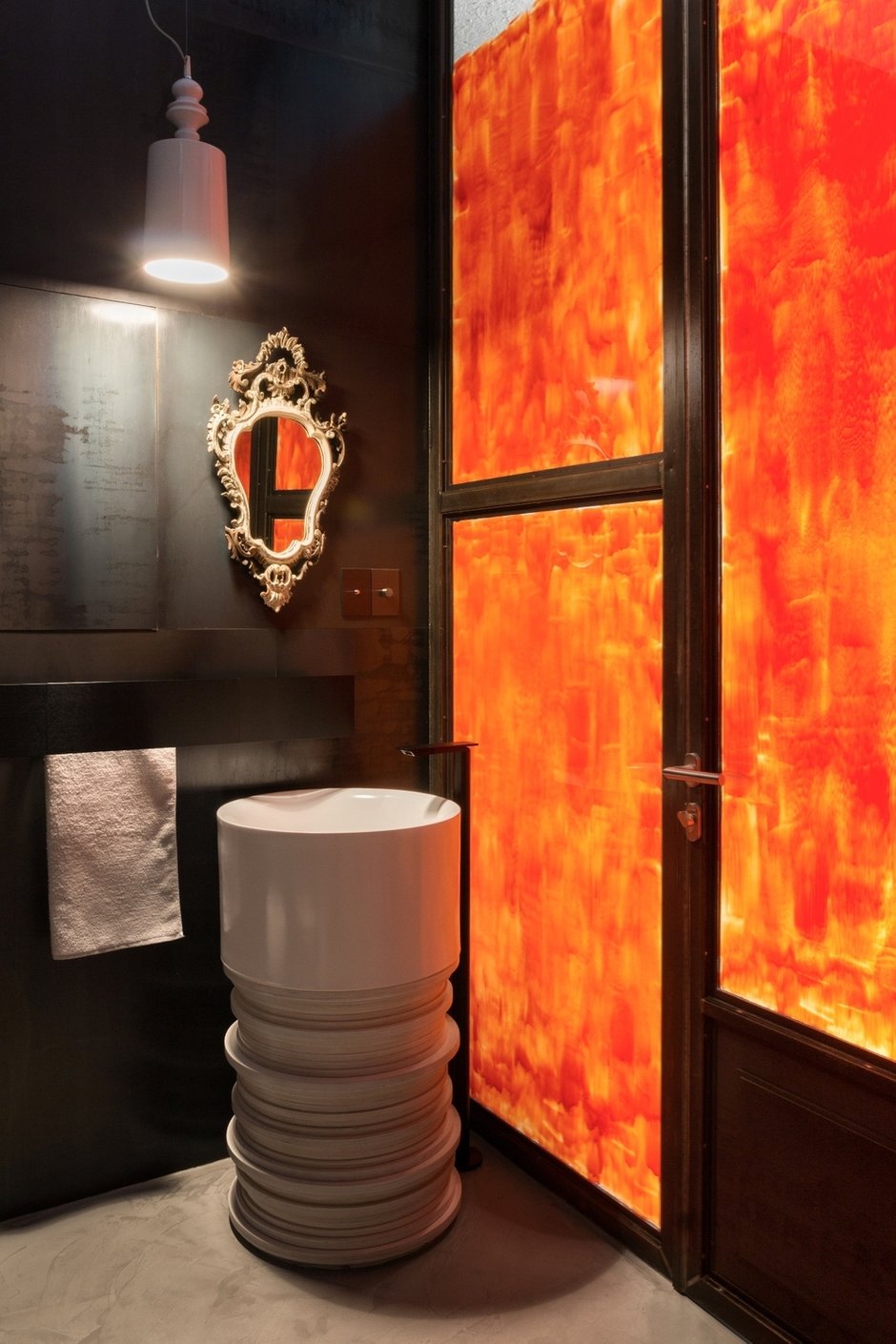 В ванной комнате использованы разные материалы: блестящая мелкоформатная плитка, черный металл и частично окрашенная в оранжевый цвет стеклянная перегородка, пропускающая солнечный свет в ванную.