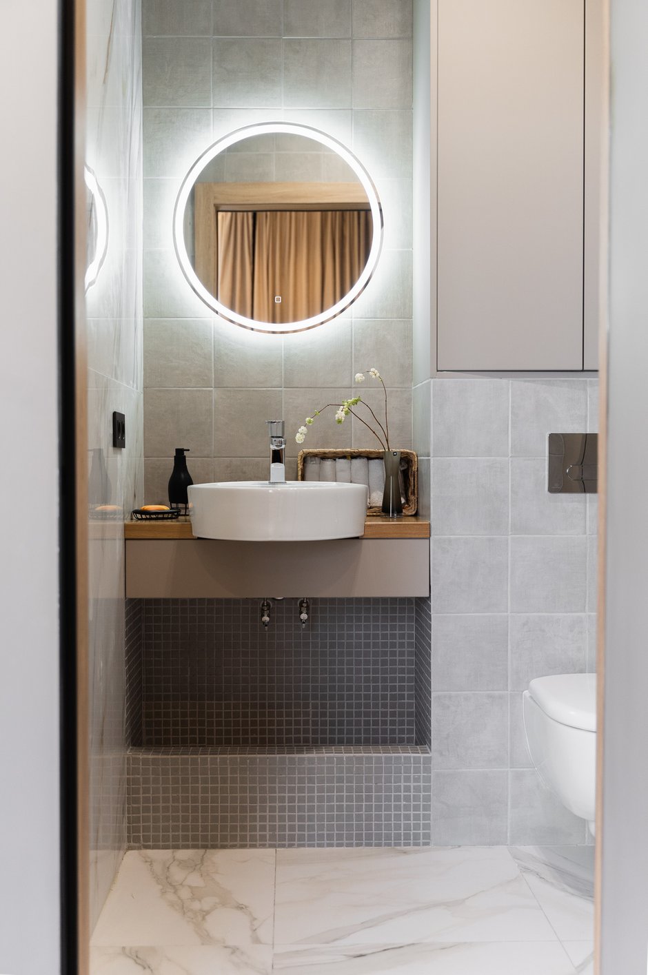 В гостевом санузле вместо полотенцесушителя сделали «теплую стену» — кабель теплого пола расположили на стене под плиткой, а сверху установили крючки для полотенец.