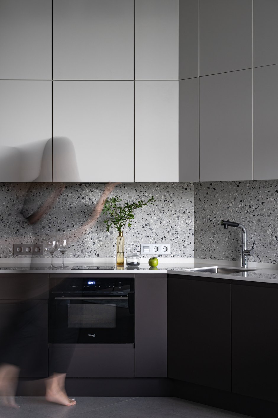 Покрытие фасадов — матовая бархатистая эмаль: выглядит очень стильно и минималистично, компенсируя незатейливую форму гарнитура. Столешница из искусственного камня, мойка из нержавеющей стали. 