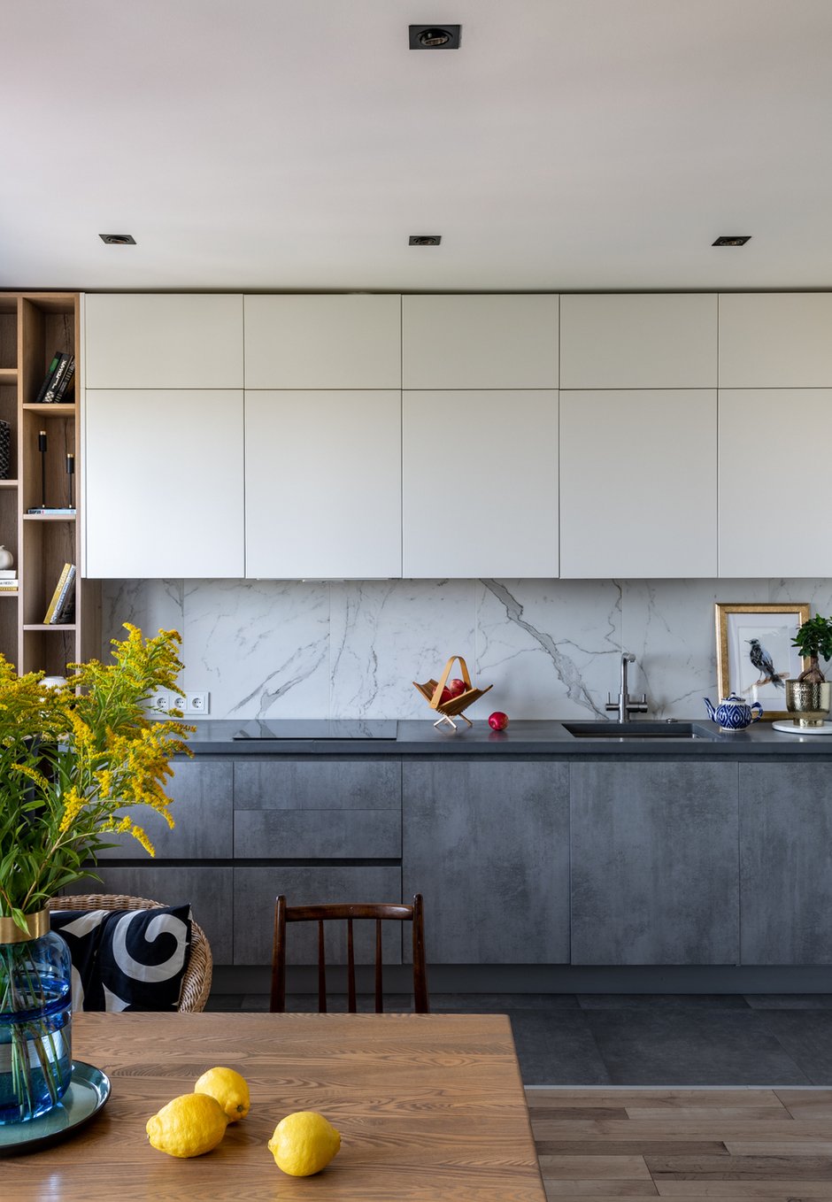 Керамогранит на фартук уложили после сборки кухни и установки столешницы. Это дало возможность поставить керамогранит прямо на столешницу и избежать стыковочного плинтуса. Чтобы сделать кухню лаконичной, отказались от мебельных ручек. Использовали систему профиля gola. Он скрыт от глаз, открывается за счет углублений над фасадами.