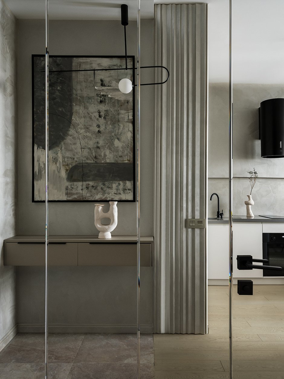 Стены оформили зеркальным панно, которое оптически расширяет пространство прихожей. Входная зона выделена керамогранитом с теплым полом. Напротив входной двери расположен шкаф для верхней одежды и обуви.