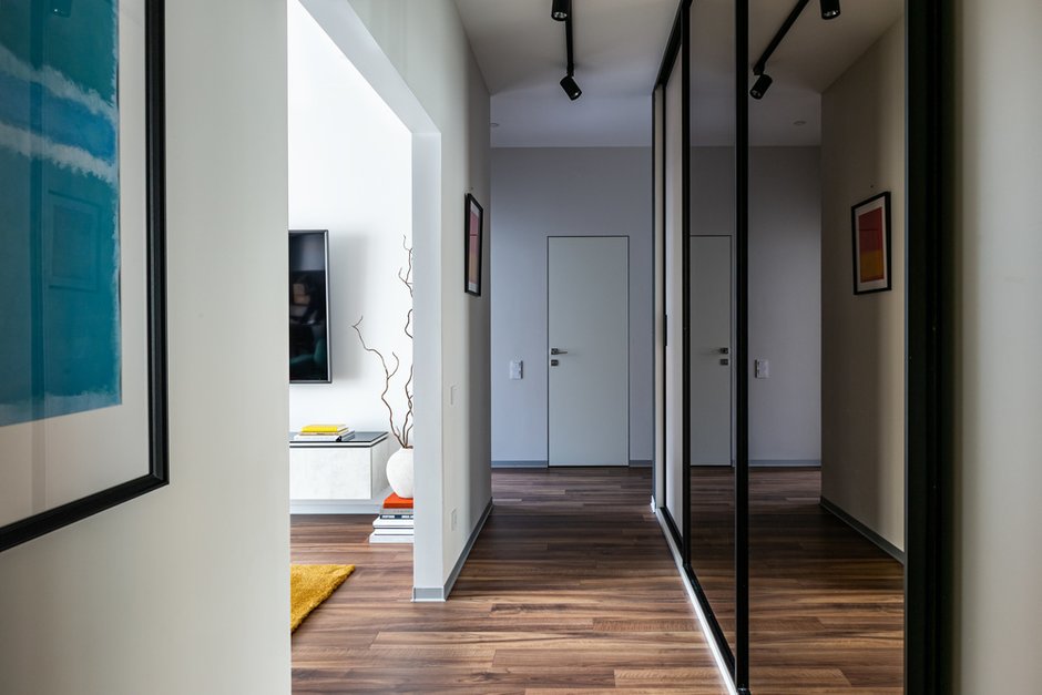 Все хранение максимально скрытое, сделано на заказ в Санкт-Петербурге. Большой зеркальный шкаф с тонированным зеркалом скрывает несколько сетов разного спортивного инвентаря: для триатлона, дайвинга, горных лыж, велоспорта. Всеми этими видами спорта профессионально занимается владелец квартиры, и это один из важных пунктов в ТЗ.