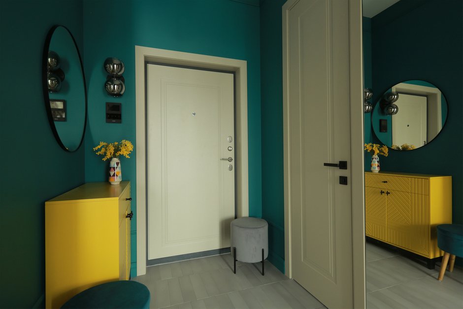 В прихожей на стене напротив гостиной появилось зеркальное панно из серебряного и бронзового зеркал: оно увеличивает освещенность прихожей, создает иллюзию каскада из подвесных светильников с красивыми сине-зелеными плафонами, добавляет красочность коридору благодаря отражению в нем гостиной.  