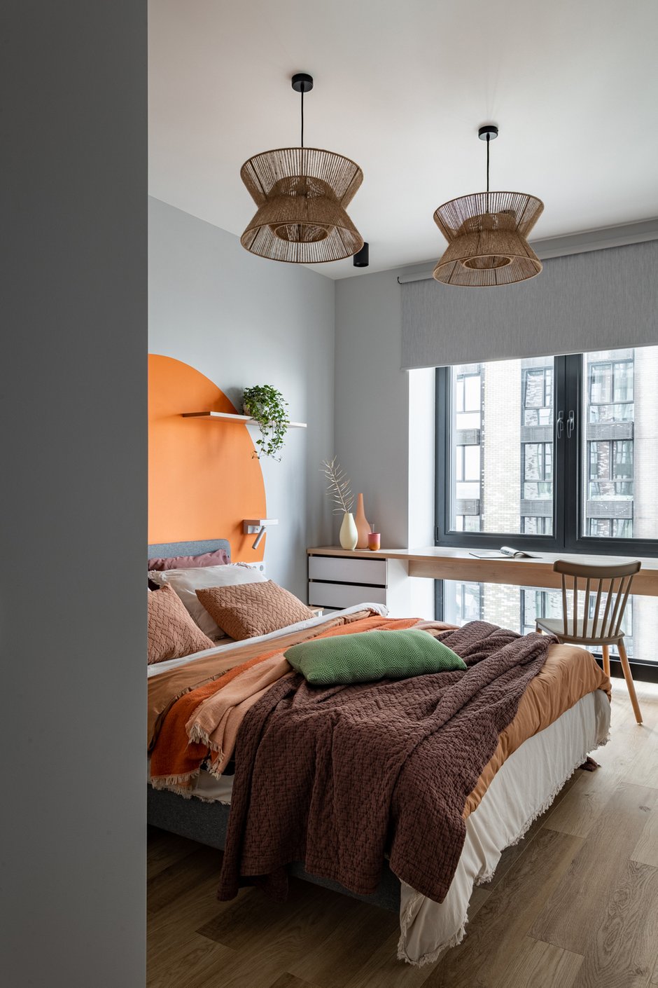 Для уюта и оживления интерьера добавили несколько растений на стеллаж и подвесную полку, а также текстиль.  Расцветка у мебели практичная: серая, в тон к стенам. Рулонные шторы использовали также серого цвета из ткани блэкаут.