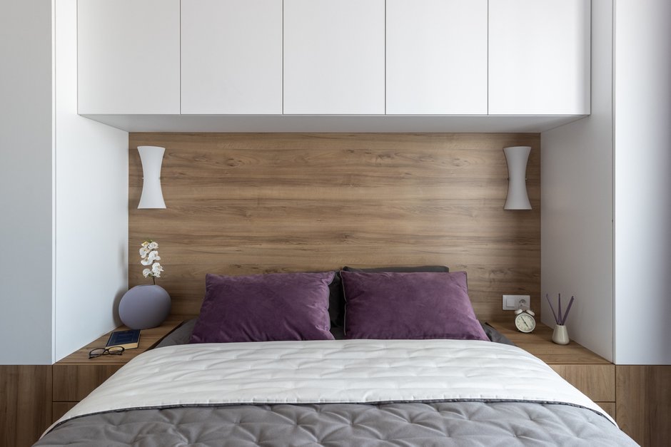 Изголовье сделали из мебельного щита, подходящего по цвету к тумбочкам и вставкам. Сюда повесили бра, поставили выключатели и розетки. Кровать, как и всю корпусную мебель, сделали на заказ.