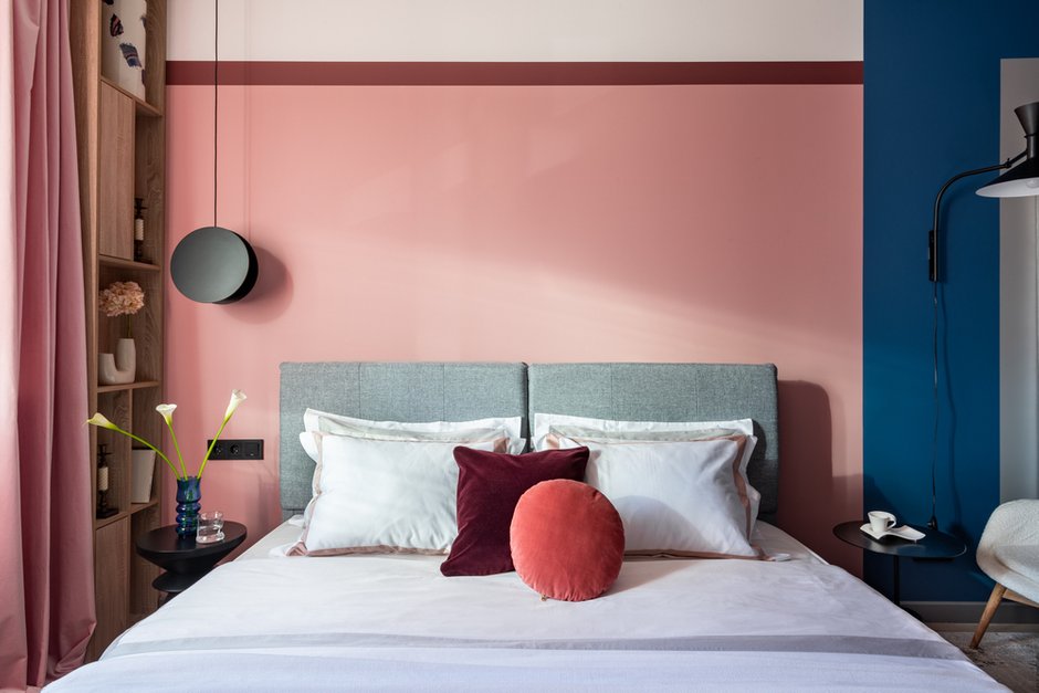 Кровать выбрали нейтрального серого цвета, постельное белье — классический белый вариант, но с элегантной цветной оторочкой на подушках, что вносит небольшой нюанс.