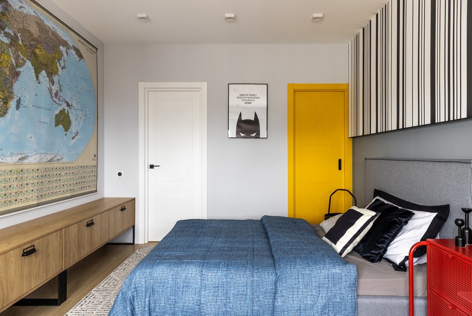 Карта мира напротив кровати вместо телевизора. Предусмотрели большой стол практически во всю стену и систему хранения для игрушек и книг. Желтая дверь задвигается в стену при открывании, за ней находится гардеробная комната.