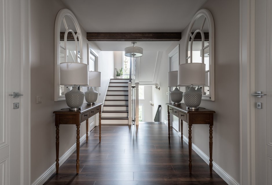 В холле на втором этаже консоли с арочными зеркалами в белых рамах и крупные настольные лампы.